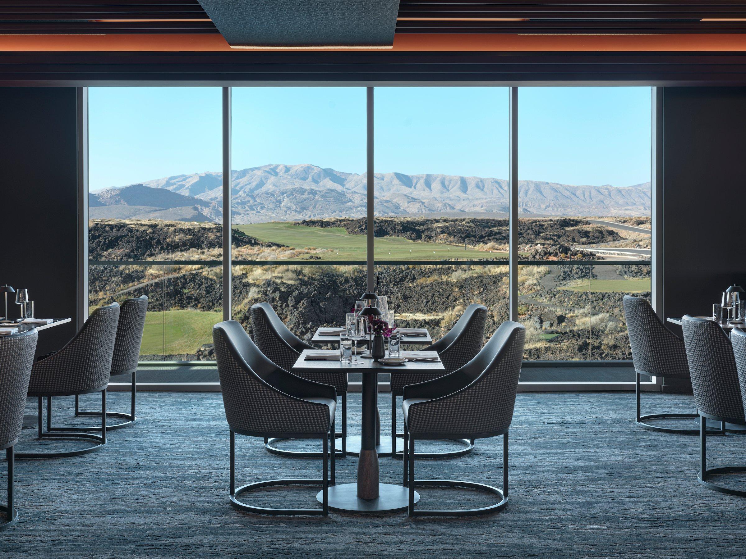 The elegant dining room of the fine dining restaurant at Black Desert Resort, featuring floor-to-ceiling windows with panoramic views of the golf course and mountains.