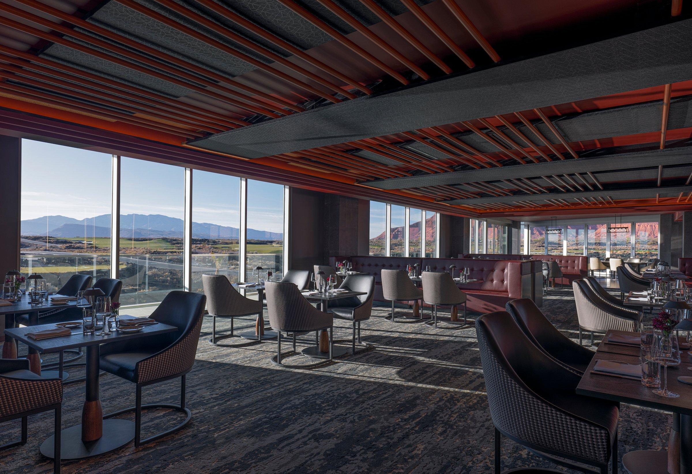 The elegant dining room of the fine dining restaurant at Black Desert Resort, featuring floor-to-ceiling windows with panoramic views of the golf course and mountains.