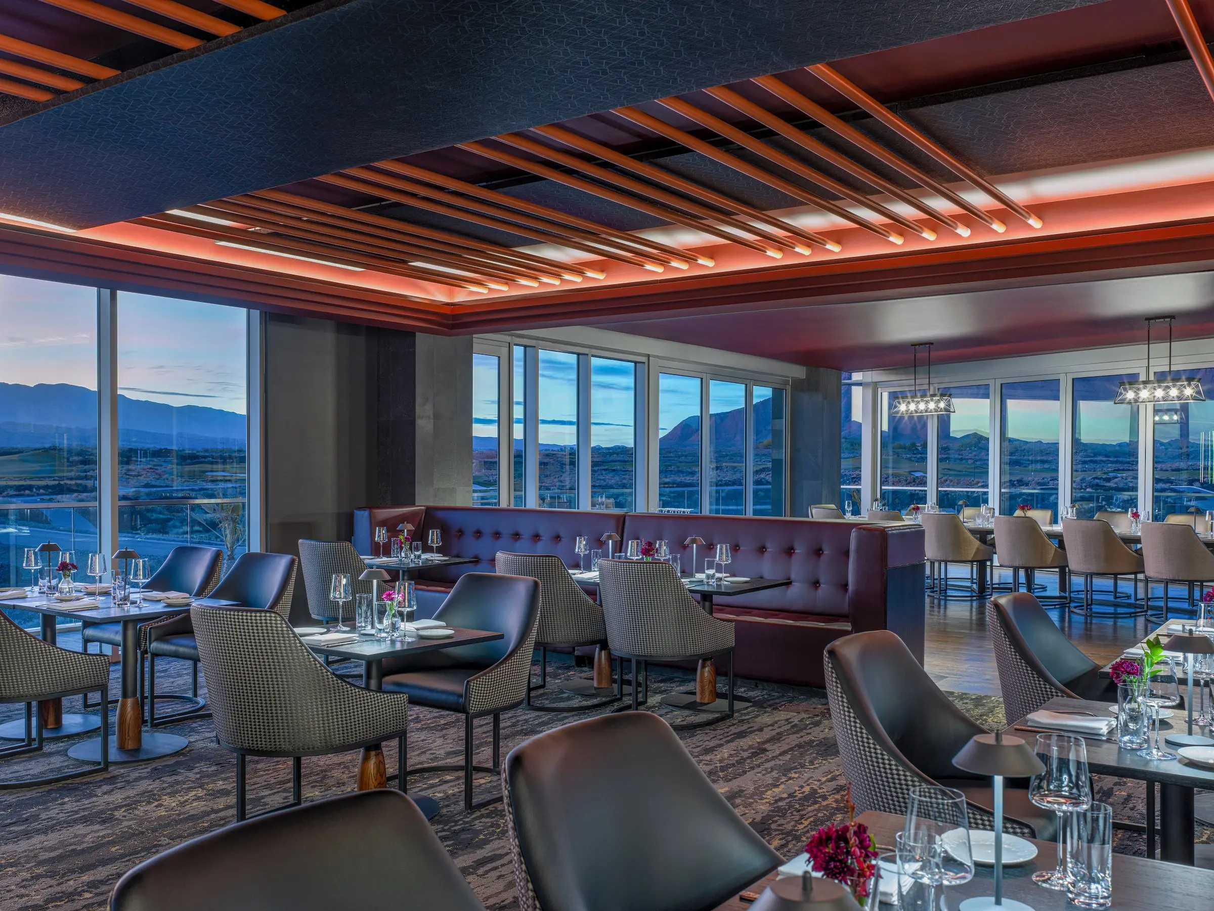 The elegant dining room of the fine dining restaurant at Black Desert Resort, featuring floor-to-ceiling windows with panoramic views of the golf course and mountains.
