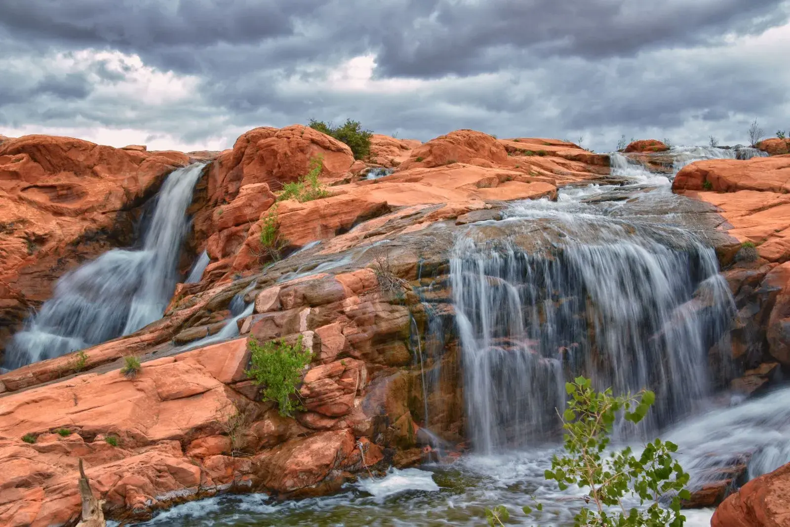 A beautiful waterfall cascading over the signature red rocks at Black Desert Resort, showcasing a unique water feature in the Utah desert.