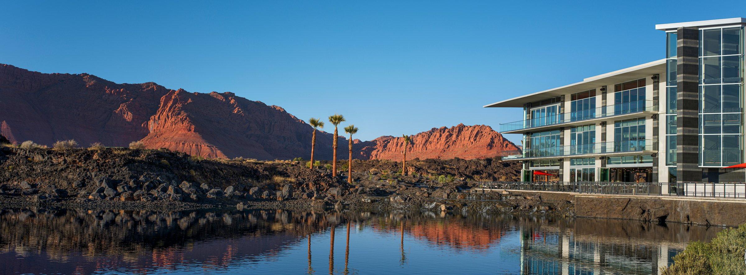 A stunning view of the modern hotel at Black Desert Resort, reflecting in the tranquil water with the iconic Utah red rock mountains in the background